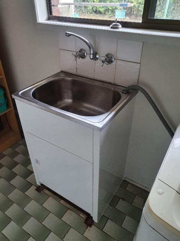 Stainless laundry trough in a white cabinet with new wall taps