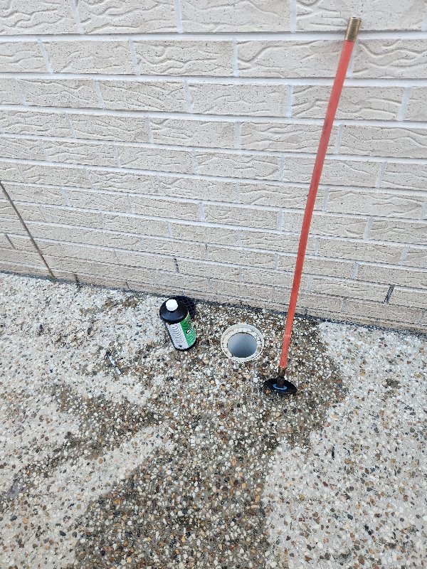 Drain rod lowered into an outdoor drain point beside a brick wall