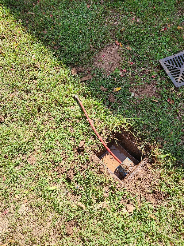 Sewer access pit dug open in a lawn with a rod in the pipe